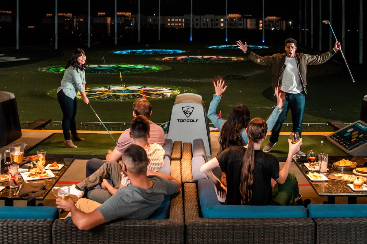 Skupina vo vlastnej Bay v Topgolfe: lounge sedačky, jedlo a nápoje, dvaja hráči pri odpalisku